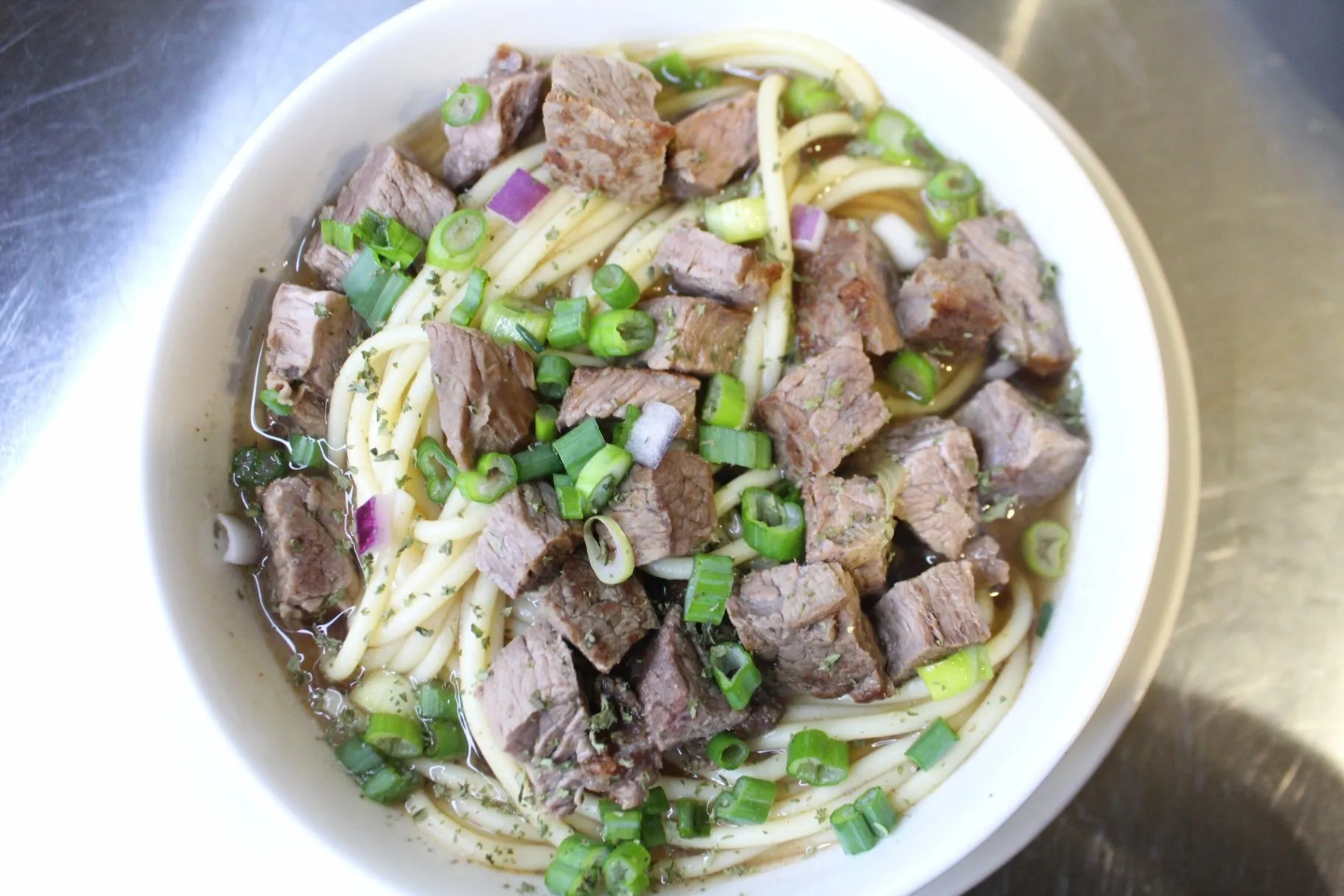 A bowl of noodles topped with beef and green onions